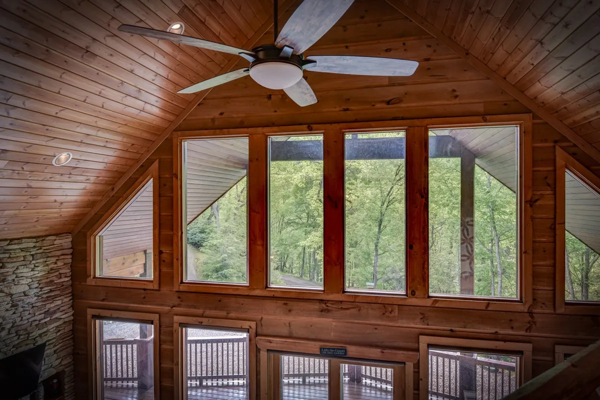 A tranquil sitting area with large windows, a wooden ceiling, and a stone wall, offering views of the surrounding nature. The space is bathed in natural light and features inviting seating that creates a peaceful retreat for relaxation or watching wildlife.