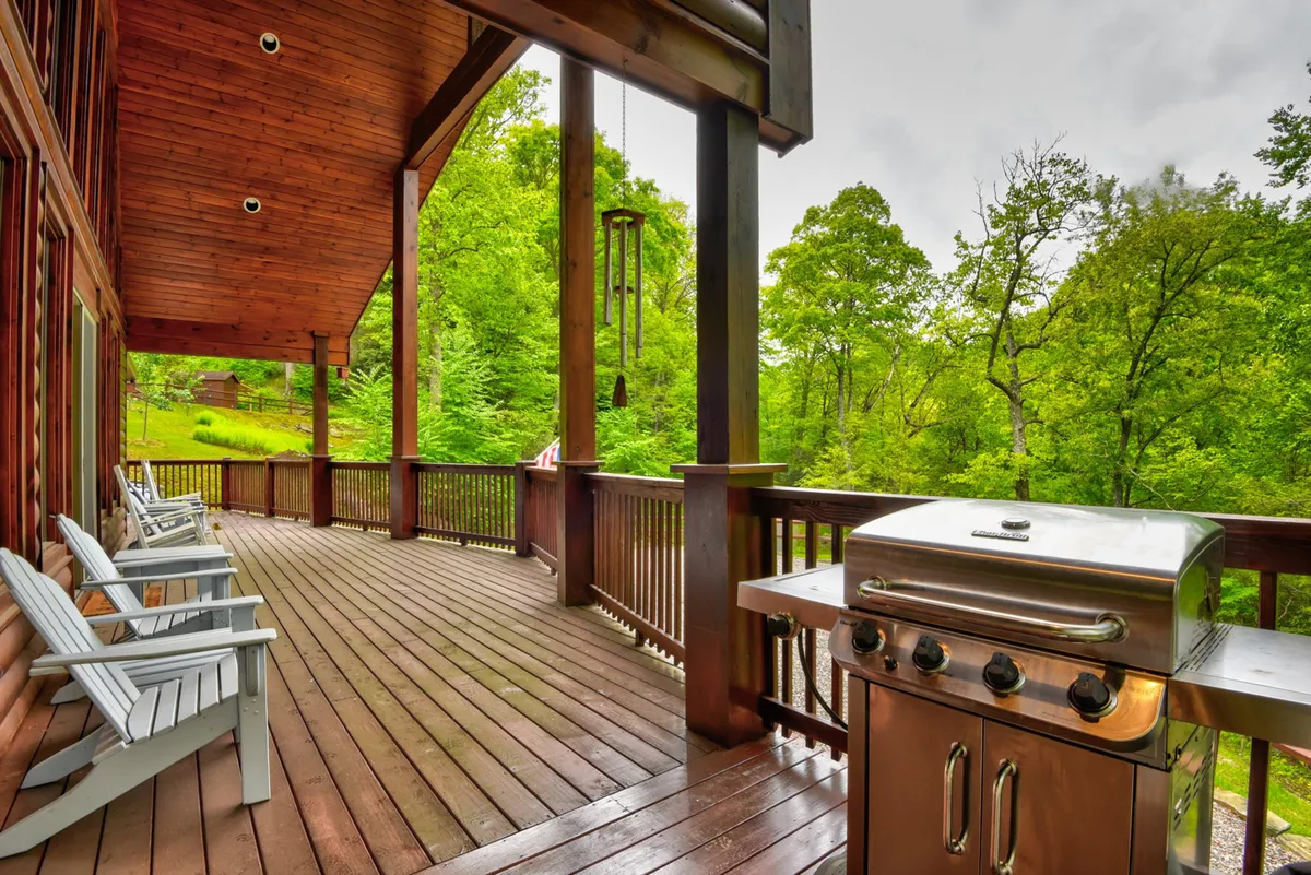 An inviting exterior deck scene featuring a wooden deck outfitted with a barbecue grill and rocking chairs, framed by lush greenery. The setup is perfect for outdoor dining, storytelling, and family gatherings after a fun day by the lake.