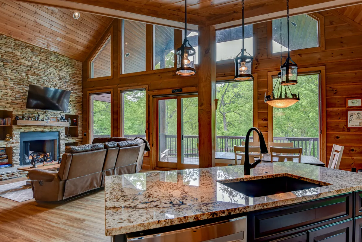 A cozy living space featuring a stone fireplace, reclining sofas, granite countertop, and large windows. The layout encourages intimate gatherings and relaxation, with visual access to the mountain scenery outside.