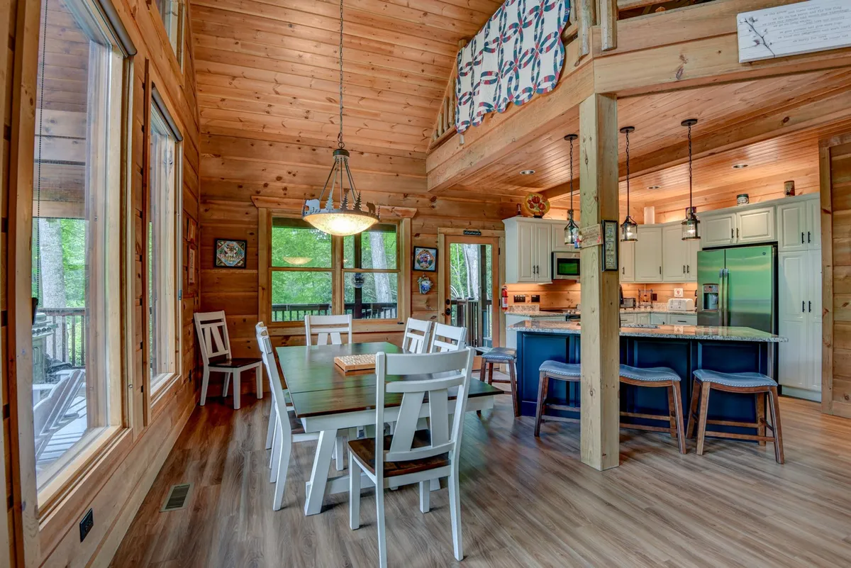 An inviting interior view of the dining area, kitchen island, and large windows, filled with warm natural light. The setup highlights the open-concept layout, perfect for family dinners, cooking together, and socializing.