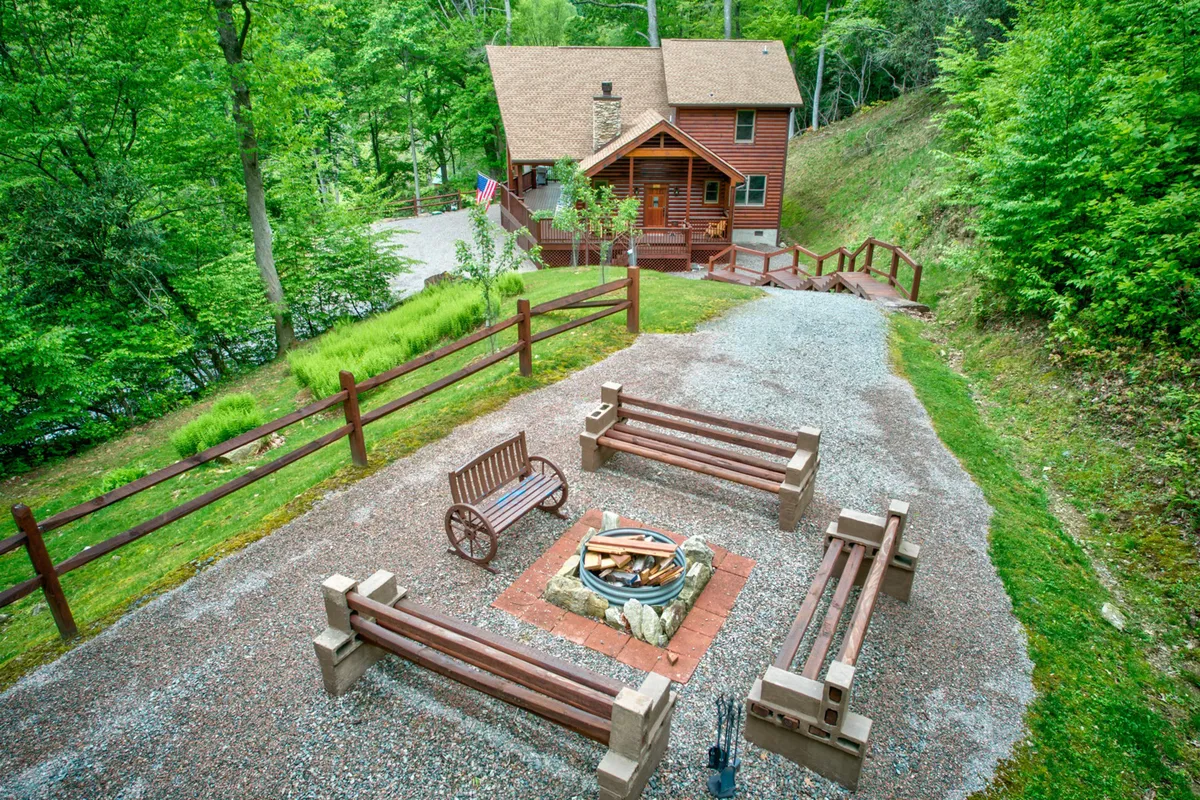 A cozy firepit area set on a well-kept lawn with rustic benches encircling the firepit. The scene is enveloped by greenery, creating a welcoming space for storytelling, making s’mores, and nighttime gatherings.