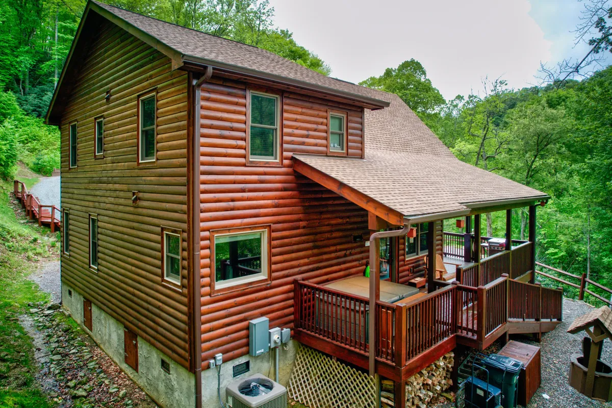 The inviting log cabin exterior featuring a spacious deck, surrounded by vibrant greenery. The deck is set up for outdoor gatherings, barbecues, or simply enjoying morning coffee with views of the mountains.