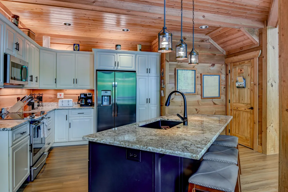 A modern kitchen equipped with a granite countertop island, stainless steel appliances, pendant lights, and wooden cabinetry. The kitchen is clearly designed for gatherings and culinary adventures, with inviting, cozy touches throughout.