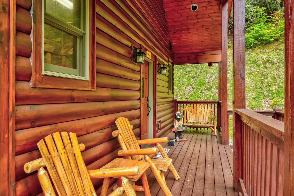 A cozy porch with wooden rocking chairs, set against the classic log cabin structure and surrounded by trees. The inviting atmosphere is perfect for relaxing after a mountain adventure, with clear sightlines to both the yard and surrounding nature.