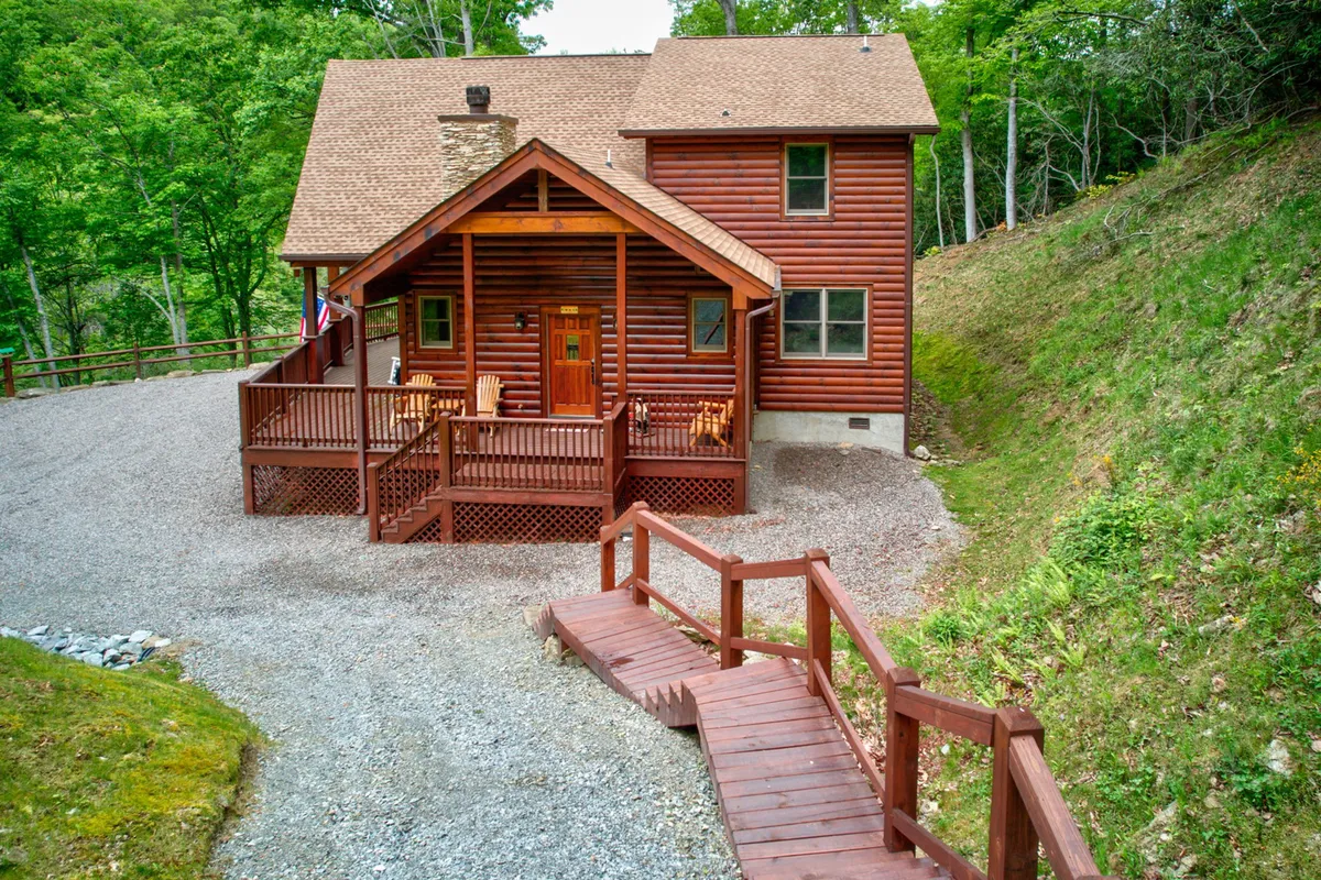 This exterior image captures the log cabin’s welcoming structure, featuring a spacious wooden deck with stone accents. The outdoor area is set up for relaxation and gatherings, making it ideal for enjoying the mountain air, morning coffees, or evening bonfires.
